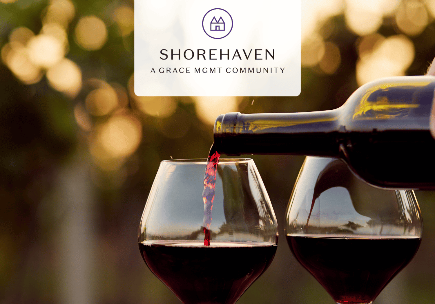 Wine being poured into two glasses outdoors with a blurred warm background; Shorehaven logo and 'A Grace Mgmt Community' overlay.