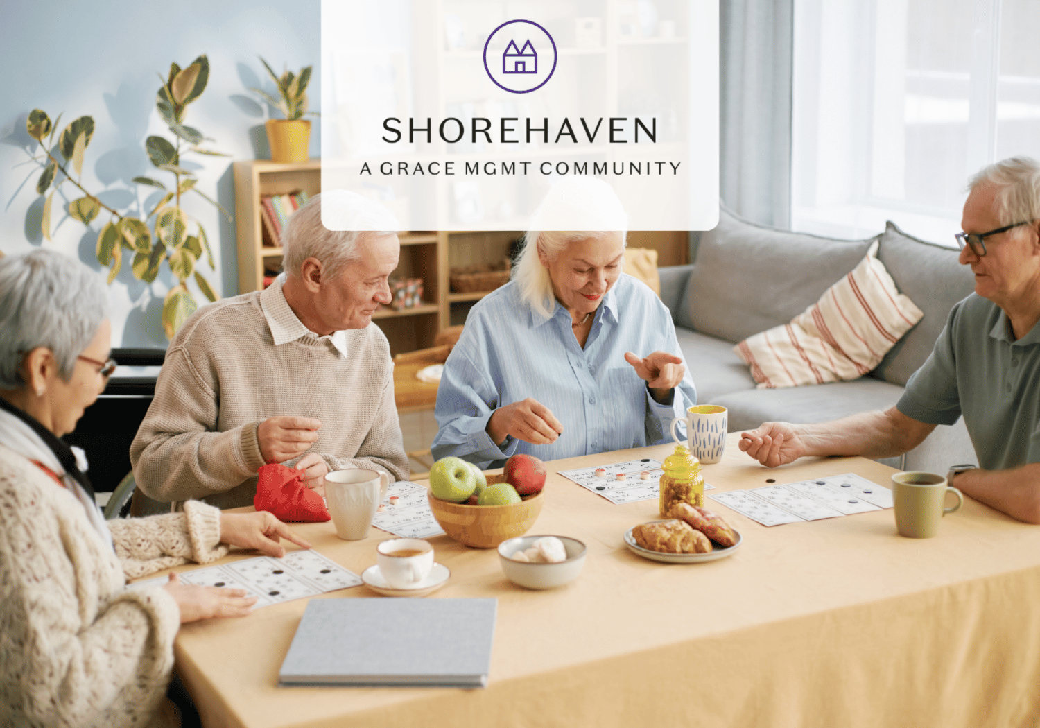 Seniors gathered around a table playing a board game, with a fruit bowl, pastries, and mugs nearby; Shorehaven logo overlay at the top.